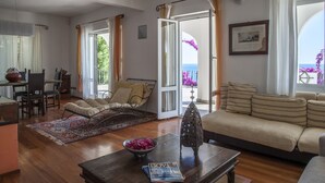 Un vaste espace de vie comprenant un canapé, une table à manger et une chaise. Une grande fenêtre, agrémentée de rideaux, offre une vue sur l’extérieur.