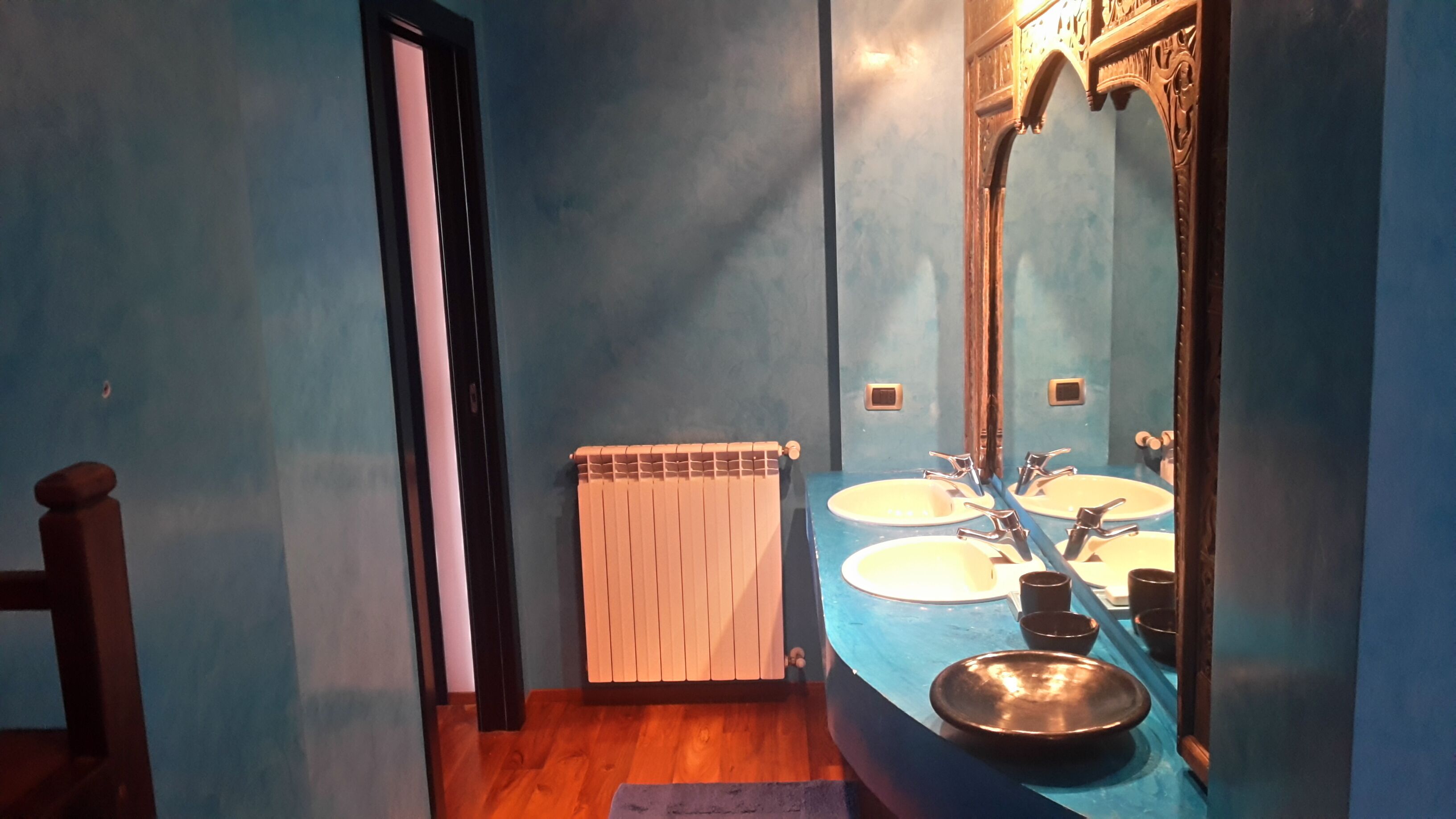 Un baño con dos lavamanos, un espejo, un radiador y suelo de madera.