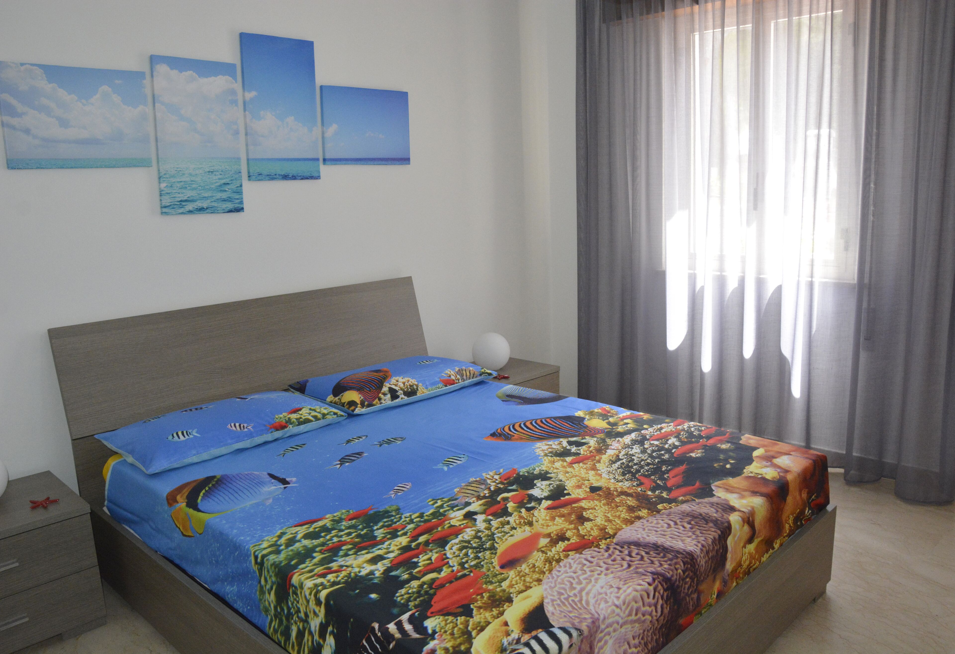 A bedroom with a bed, a nightstand, and a wall with three framed pictures.