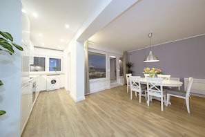 A modern kitchen with a built-in washing machine, a dining area with a table and chairs, and a large window with a view.