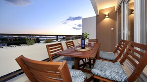 A wooden dining table with chairs, a bottle, and glasses on a balcony with a view of the sea. - PORAT Apartment-Breathtaking sunset view in Zadar, Croatia (Zadar)