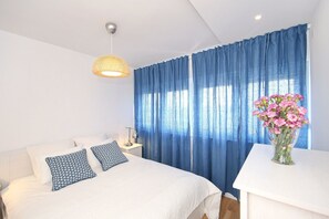 A bedroom with a bed, a bedside table, a lamp, a vase with flowers, and a window with blue curtains.