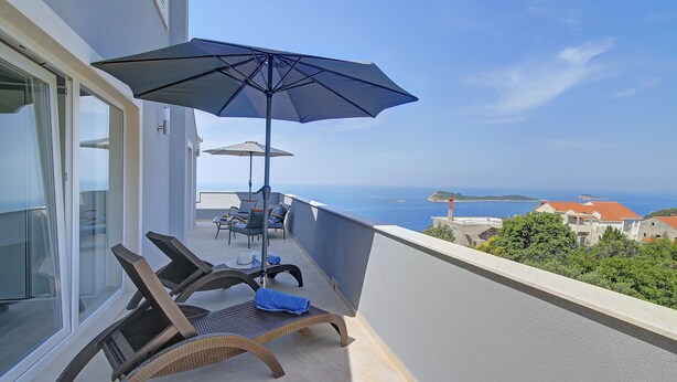 A balcony with wicker lounge chairs, a blue umbrella, and a view of the sea.
