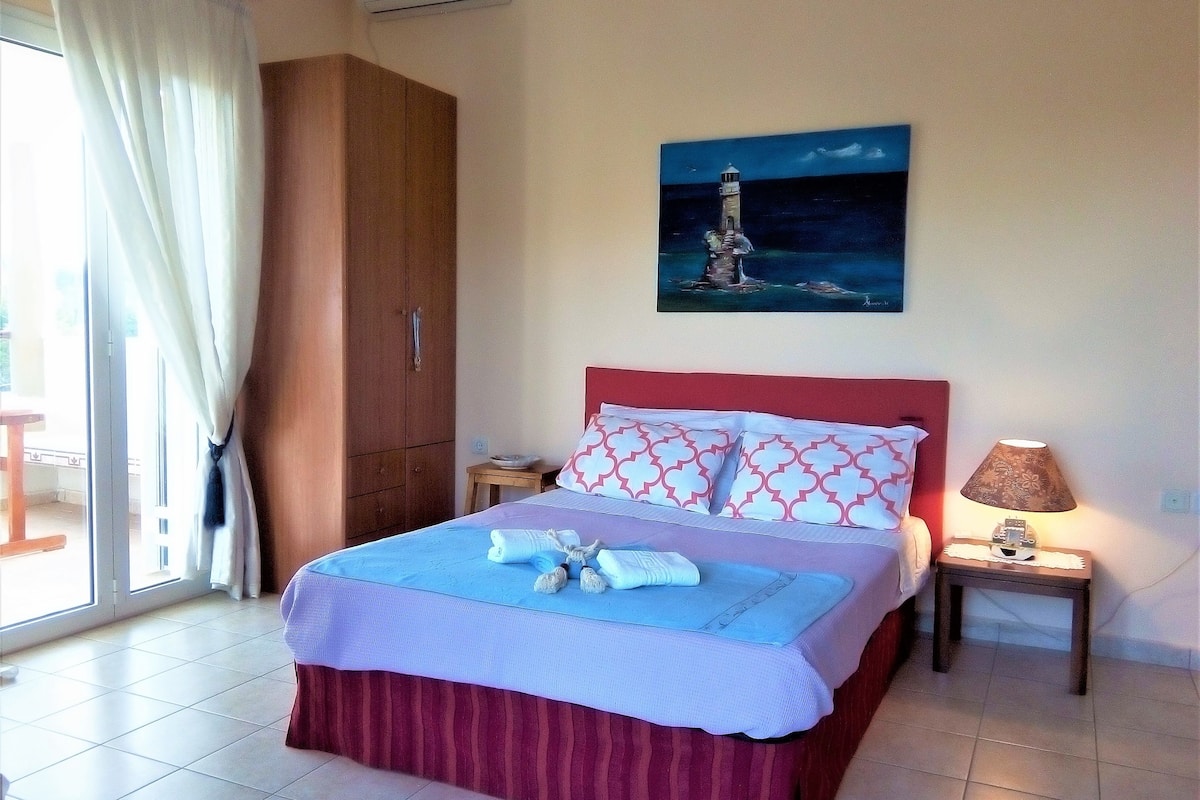 A bedroom with a bed, a nightstand, a lamp, a wardrobe, and a painting of a lighthouse.