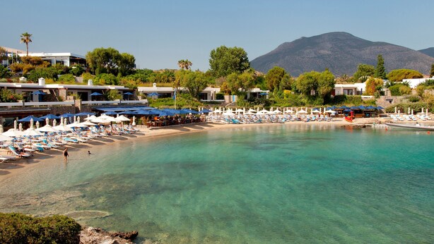 A beach resort with clear turquoise waters, sun loungers, umbrellas, and a mountain backdrop. - Angelina's Home (Saronikos)