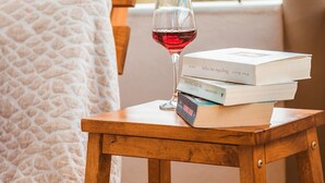 A wooden side table with a glass of red wine and a stack of books. - Angelina's Home (Saronikos)