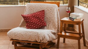 A balcony with a cushioned chair, a small wooden table, and a glass of red wine. - Angelina's Home (Saronikos)