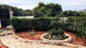 A stone pathway leading to a garden with various plants and a fenced area. - Angelina's Home (Saronikos)