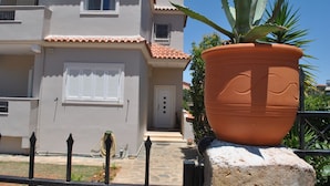 A two-story building with a tiled roof, a large potted plant in front, and a small garden area. - Angelina's Home (Saronikos)