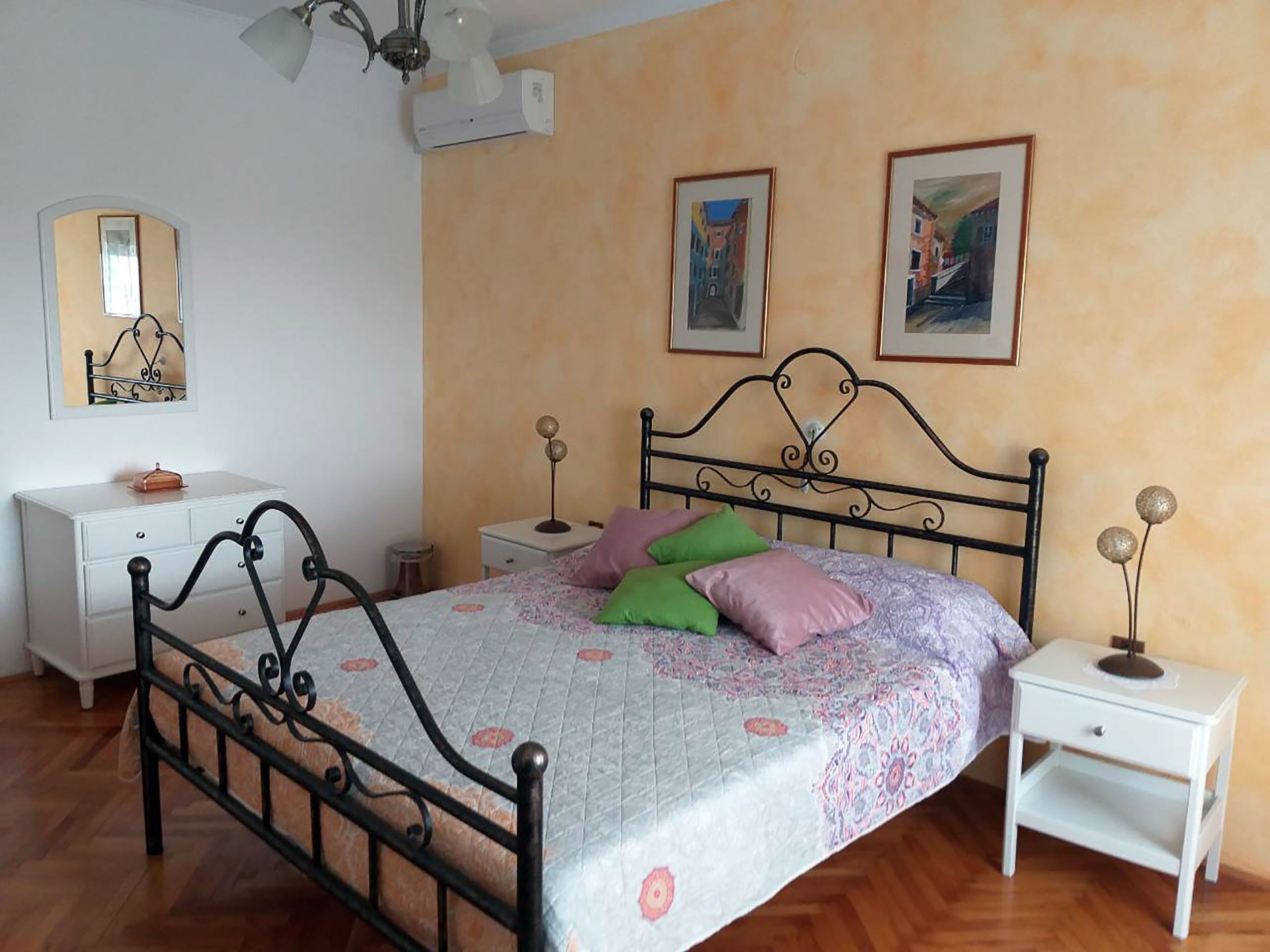 Un dormitorio con cama, mesitas de noche, un armario y dos cuadros en la pared.