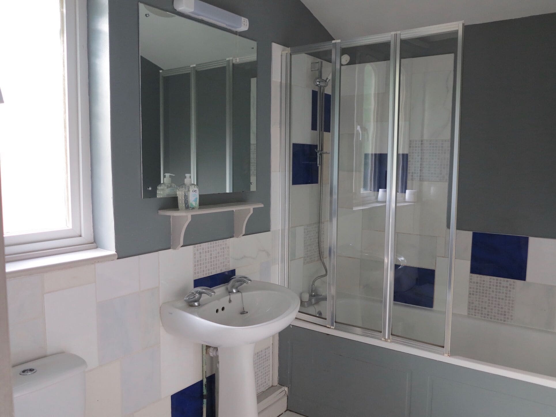 A bathroom with a glass-enclosed shower, a white sink, and a mirror above it.