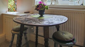 A room with a round table, two stools, a window with a view of the outside, and a decorative vase with flowers. - 'Oh So Snug' Bijou 1-bedroom cottage, in the heart of Whalley, Clitheroe  (Whalley)