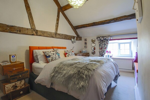 Een slaapkamer met een bed, houten balken, een raam en een dressoir.