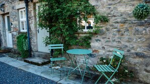 A stone building with a small outdoor seating area featuring two green metal chairs and a round table. - 'Oh So Snug' Bijou 1-bedroom cottage, in the heart of Whalley, Clitheroe  (Whalley)