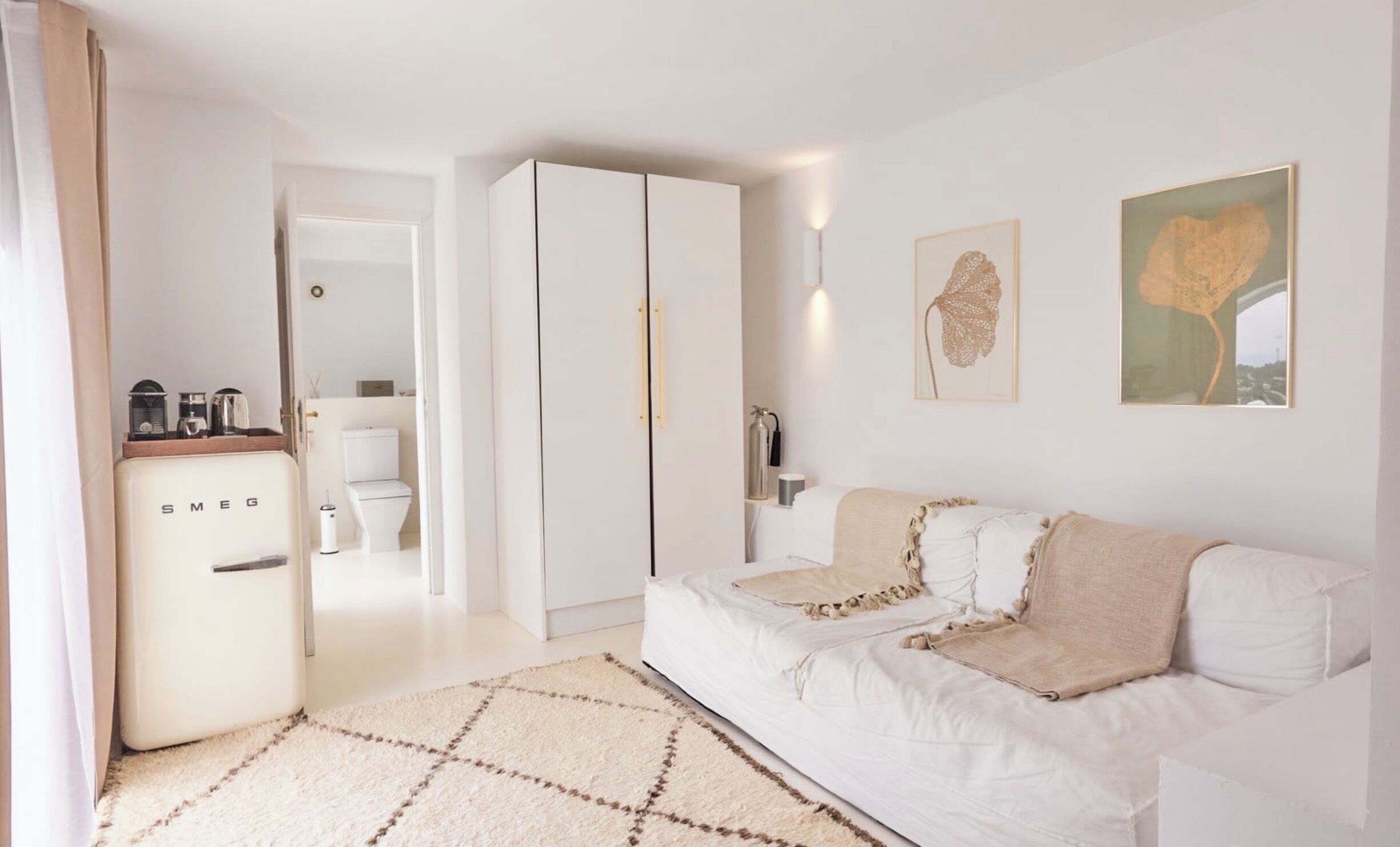 Un dormitorio moderno y minimalista con un sofá blanco, una alfombra estampada y un armario.