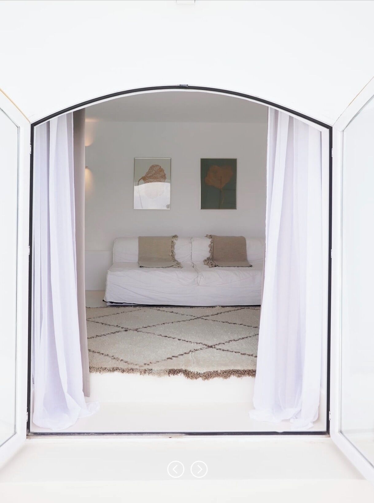 Un dormitorio con cama, cortinas blancas y dos cuadros en la pared.