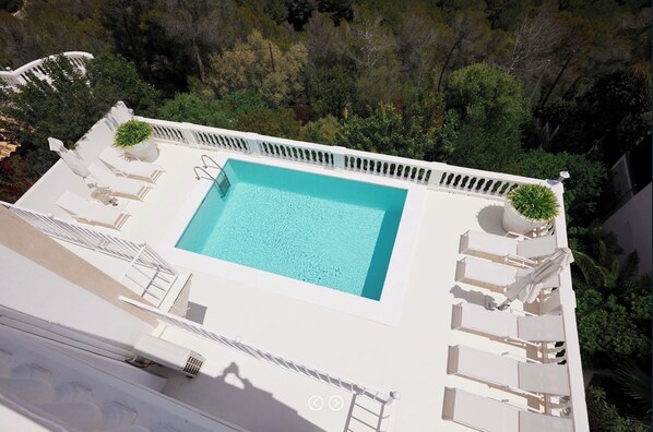 Une piscine sur le toit, avec une eau d’un bleu cristallin, entourée de chaises longues blanches et de plantes en pot.
