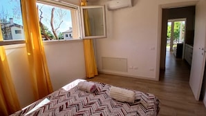 Et soveværelse med seng, et vindue med gardiner, en aircondition og udsigt ud.