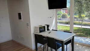 Et moderne værelse med spisebord, stole, et fladskærms-tv ophængt på væggen og et vindue med udsigt.