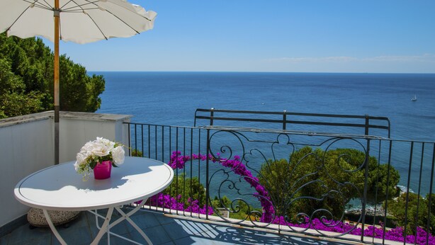 A balcony with a white table, a pink vase with flowers, and a white umbrella.