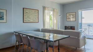 A room with a dining table, chairs, a sofa, and a balcony with a railing.