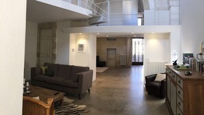 Uma sala de estar ampla com teto alto, escada para um andar superior, lareira e uma coleção de livros e objetos decorativos.