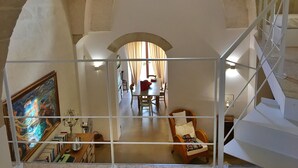 Um quarto espaçoso com teto alto abobadado, uma escadaria e uma área de jantar visível através de um arco.