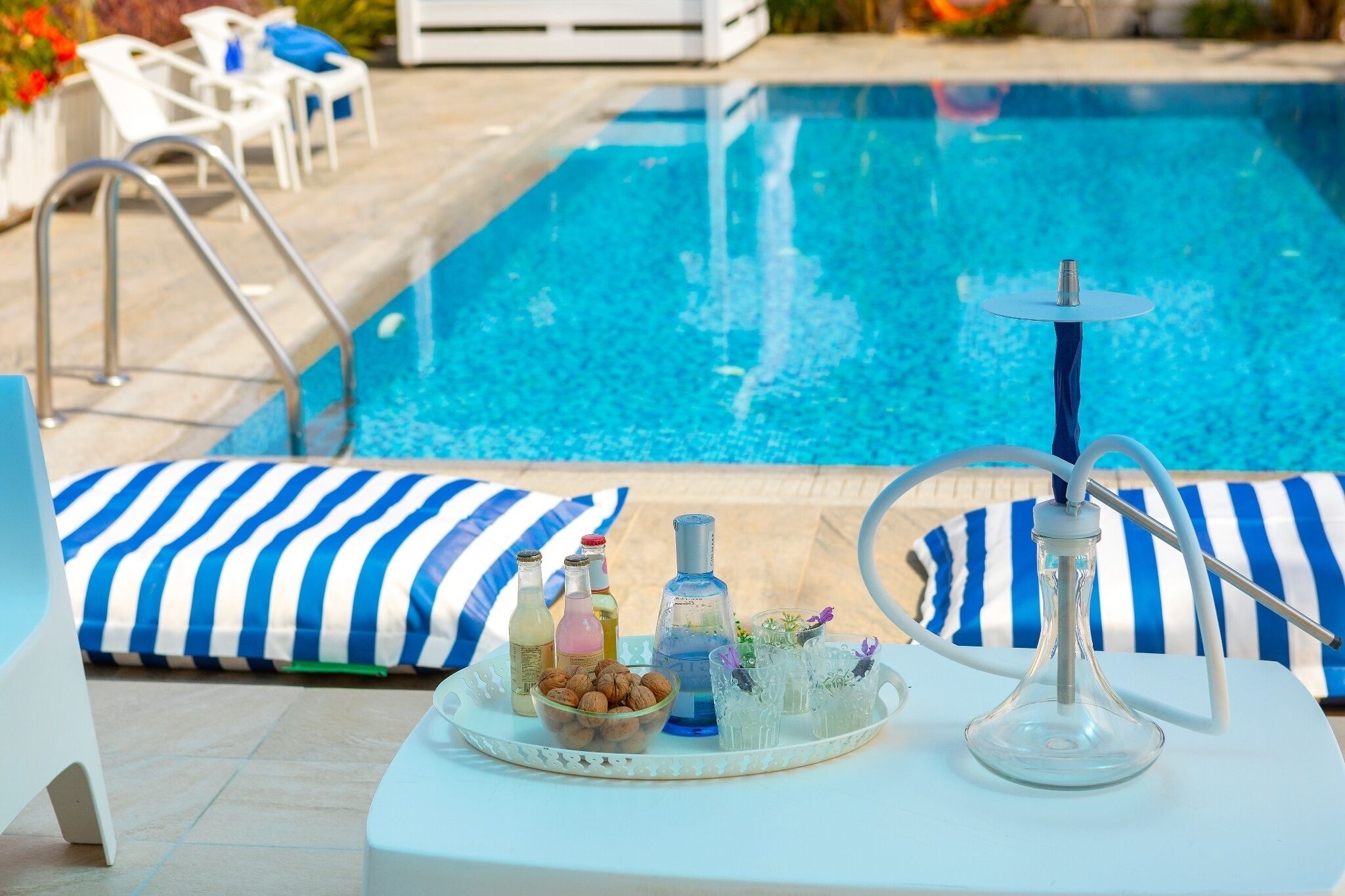 A poolside setting with lounge chairs, a tray with drinks and snacks, and a hookah.