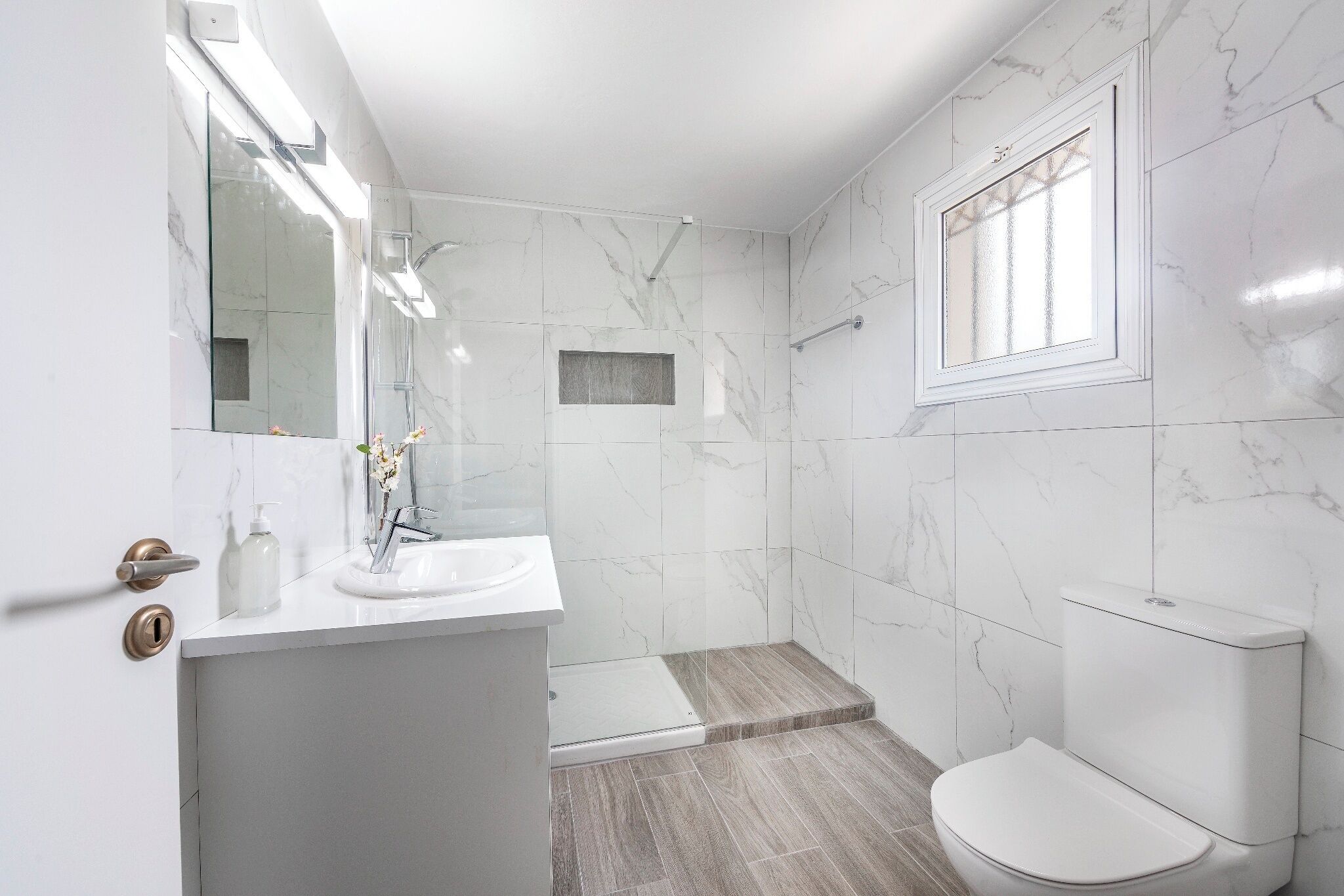 A modern bathroom with a white sink, mirror, and toilet.