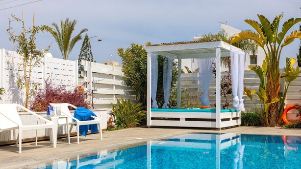 A pool area with a cabana, white lounge chairs, and a clear blue pool. - This amazing luxury villa is located in the heart of Protaras just 4 minutes walk to the Main Strip (Protaras)