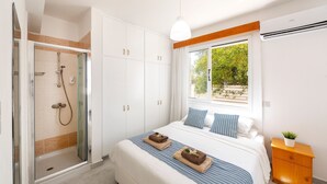 A bedroom with a bed, a nightstand, a window with a view, a shower area, and a wardrobe. - This amazing luxury villa is located in the heart of Protaras just 4 minutes walk to the Main Strip (Protaras)