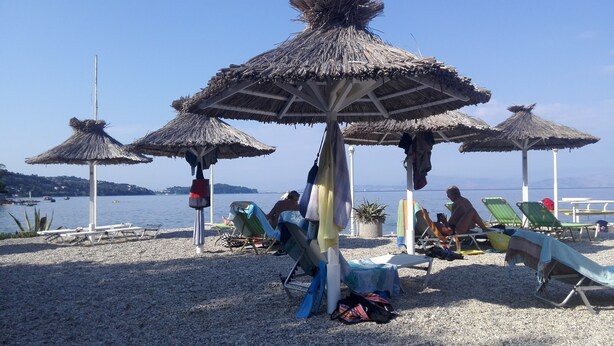 A beach with thatched umbrellas, sun loungers, and a calm sea. - Spacious,holiday house close to beach ideal for a group of friends or family (Gastouri)