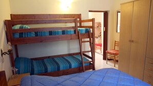 Una cama individual superpuesta con colchón azul y una escalera de madera. Hay un armario de madera y una silla en la habitación.