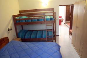 A bunk bed with a ladder, a wardrobe, and a red chair in a room with a tiled floor.