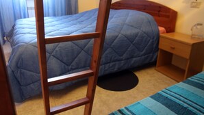 Un dormitorio con escalera de madera, cama acolchada azul, mesita de noche y mesita auxiliar.