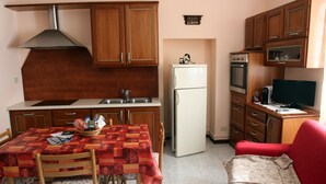 Cocina compacta con armarios de madera, un refrigerador, una estufa y una mesa de comedor con sillas.