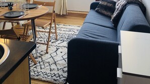 Un salon chaleureux avec un canapé bleu, une table à manger entourée de chaises et une grande fenêtre agrémentée de rideaux.