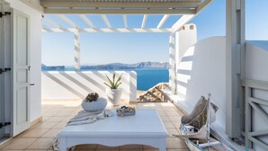 A balcony with a white table, potted plants, and a view of the sea and mountains.