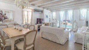 A spacious room with a wooden dining table, a white sofa, and a large window offering a view of the sea.