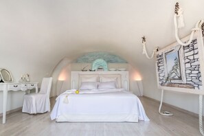 Une chambre avec un lit blanc, une chaise blanche, un bureau avec un miroir et un tableau encadré au mur.