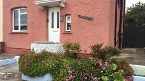 Una casa rosa con una puerta blanca, un pequeño jardín con flores rosas y un muro azul.