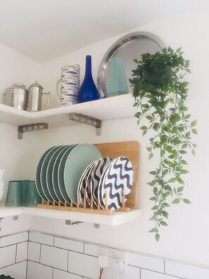 Ein Küchenregal mit Tellern, einer blauen Vase und einer hängenden Pflanze.