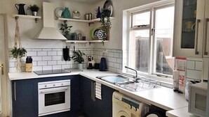 Una cocina compacta con armarios blancos y azul oscuro, horno integrado, pileta y ventana.