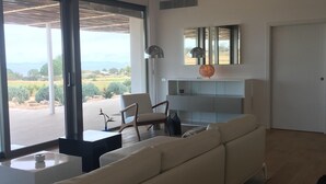 A spacious living room with a large sofa, a coffee table, and a chair. There is a large window offering a view of the outdoors. - HOUSE IN PARADISE ISLAND (El Pilar de la Mola Formentera)