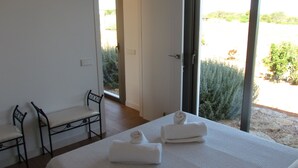 A bedroom with a bed, two chairs, and a view of greenery outside. - HOUSE IN PARADISE ISLAND (El Pilar de la Mola Formentera)