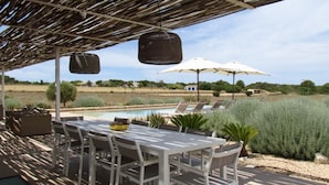 An outdoor pool area with lounge chairs and umbrellas, surrounded by greenery and a clear sky. - HOUSE IN PARADISE ISLAND (El Pilar de la Mola Formentera)