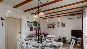 Un comedor con sillas blancas y una mesa dispuesta para cuatro personas, una araña y un televisor al fondo.