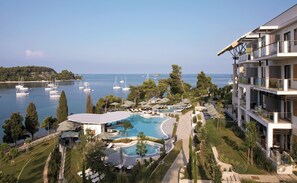 Un resort con piscina, sillas de descanso y vista al mar con barcos.