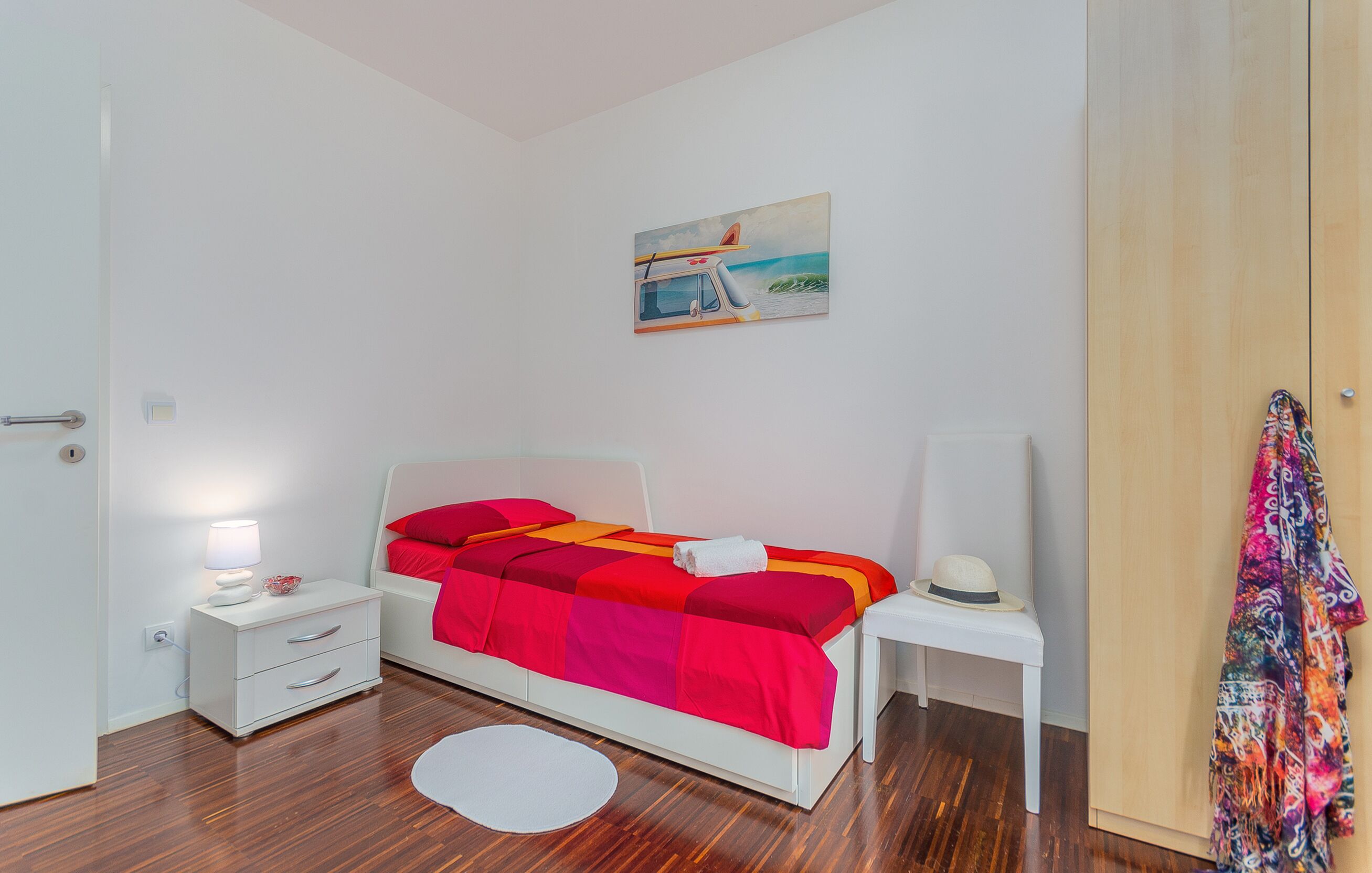 A bedroom with a bed, bedside tables, a nightstand, a painting, and a door.
