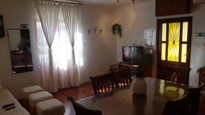 A dining area with a wooden table, chairs, and a television. There is a window with curtains, a potted plant, and a wall-mounted mirror. - A1 Large, Two bedroom Apartment of the Villa Sonia and  Teo, Hvar, Croatia (Hvar)